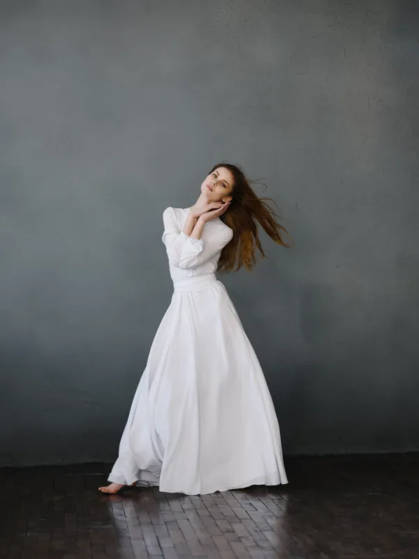 Красивая женщина в белом платье позирует в полный рост в студии