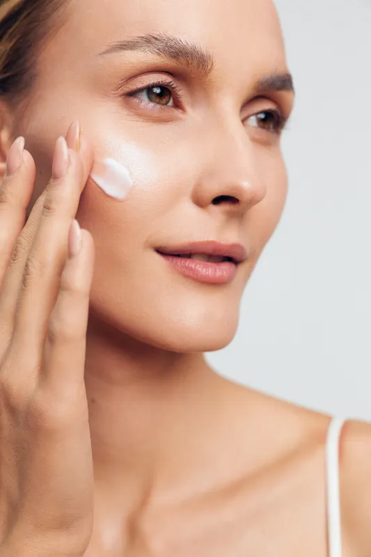 Woman applying white face cream in a closeup on clean background. Skincare and wellness concept with soft studio lighting and calm self care.