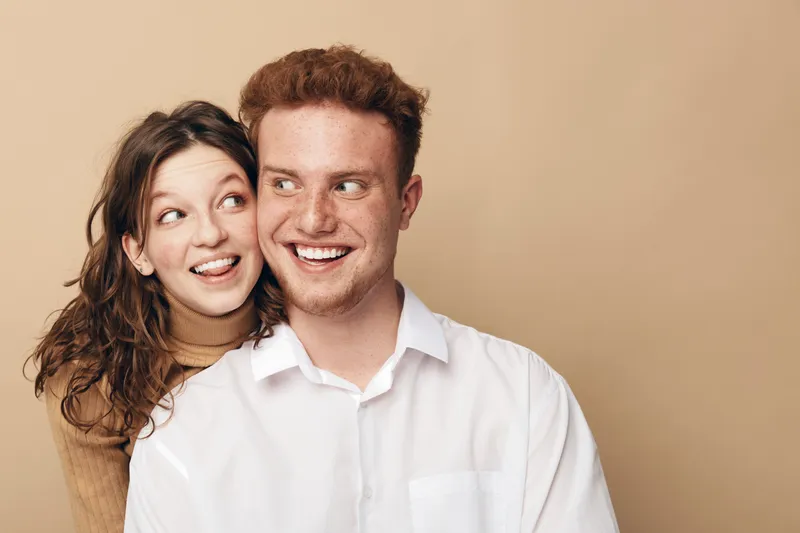 Happy young couple with red hair and curly hair smiling and looking away on beige background. Concept of friendship, love, and positive emotions in casual style.