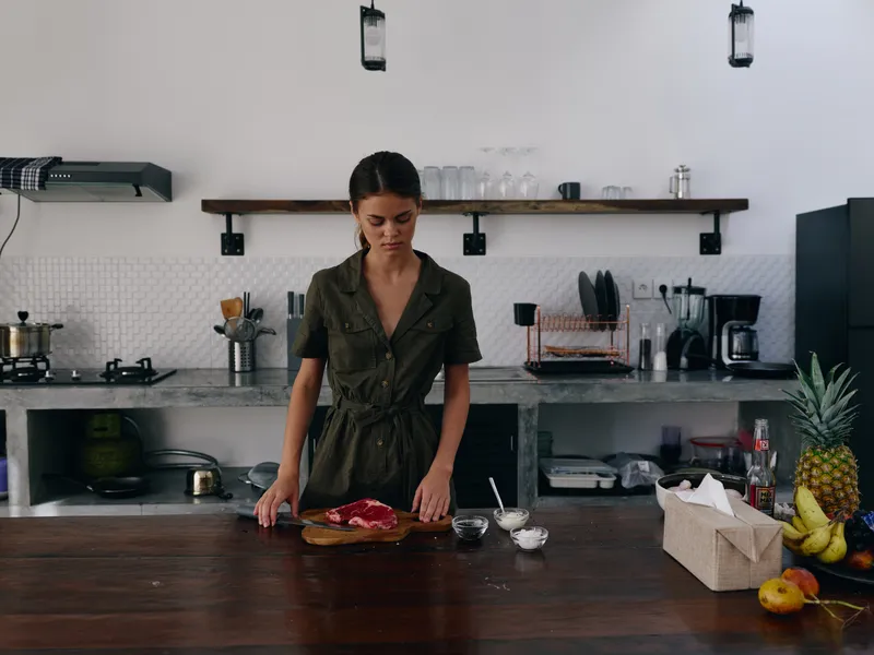 Женщина готовит мясо для запекания дома на кухне, на столе овощи и специи