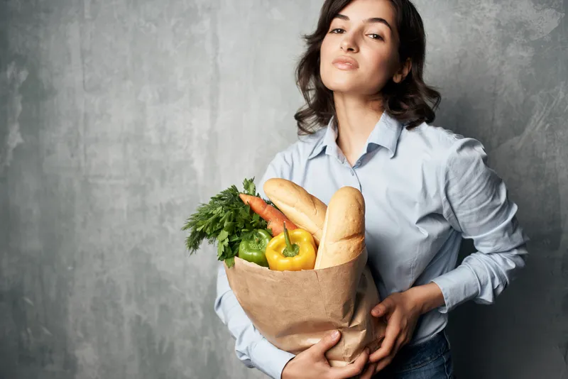 Женщина держит пакет с продуктами здорового питания, овощами в супермаркете