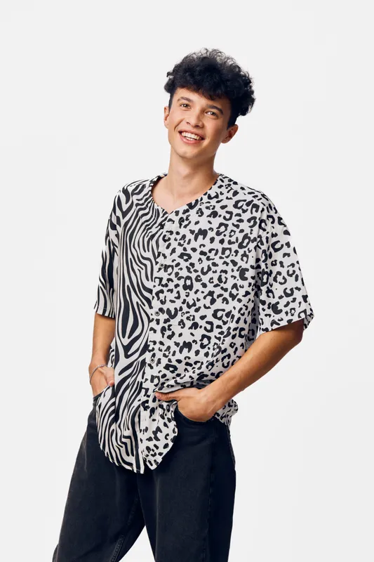 young man smiling wearing a black and white animal print shirt with casual black pants posing with hand in pocket on white background