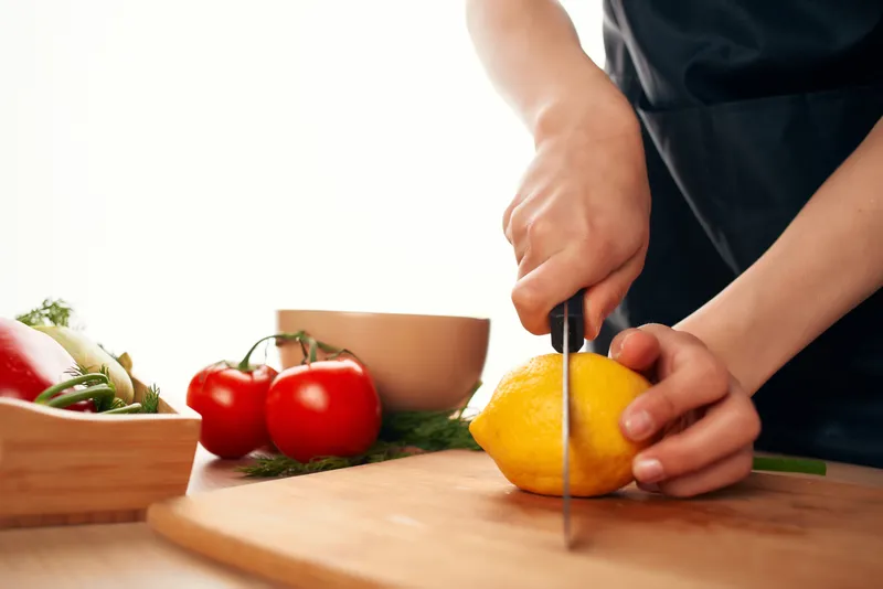Повар с ножом в руках нарезает овощи и лимон на кухне