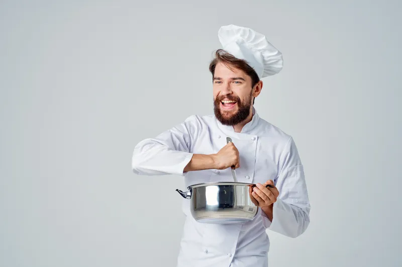 Повар готовит еду в кастрюле на кухне, занимаясь приготовлением пищи
