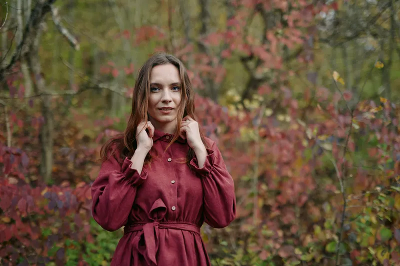 Close portrait of a woman in a burgundy dress amid autumn woods, capturing authenticity and natural presence with reliable, accurate detail that highlights genuine emotion, subtle smile and soft