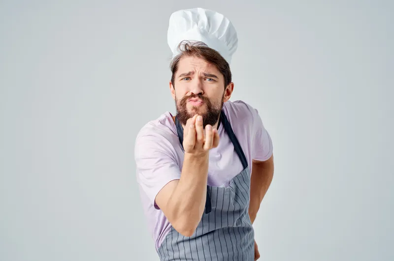 Мужчина в поварской форме готовит на профессиональной кухне ресторана
