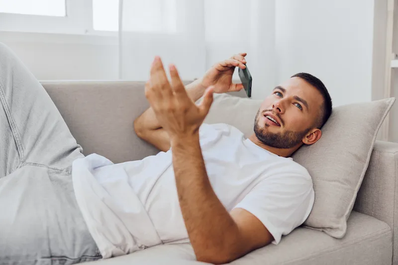 Relaxed man talking on the phone while lounging on a cozy sofa, expressing thoughtful emotions and engaging in a vibrant conversation indoors with natural light.