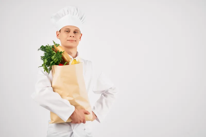 Мужчина в поварской форме с пакетом продуктов на работе в ресторане