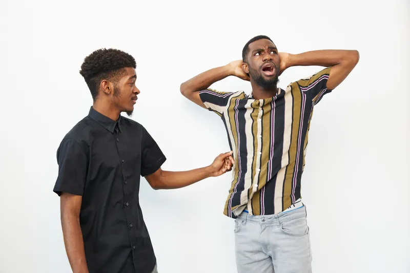 Two African American men interacting playfully, showcasing a joyful moment. Their vibrant outfits reflect a lively atmosphere, bringing energy to the scene.