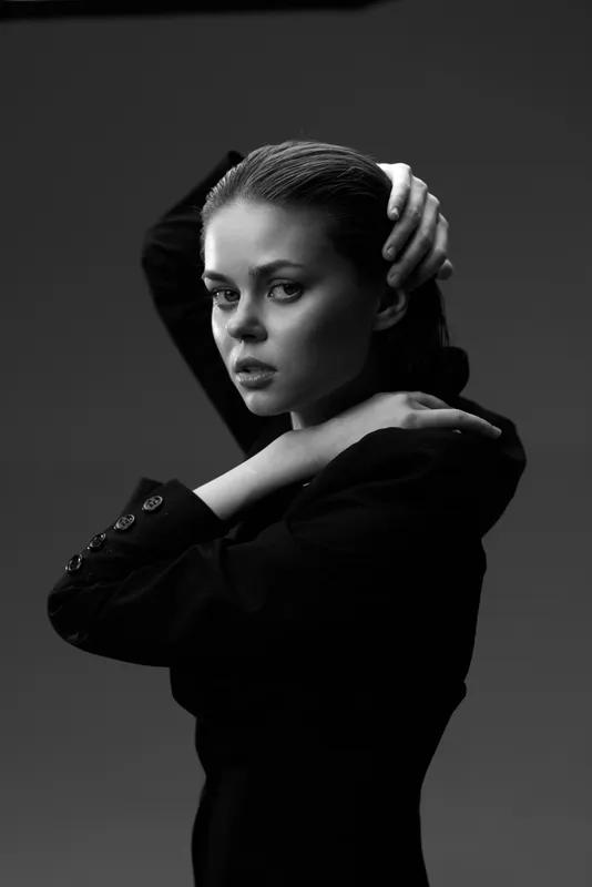 Black and white portrait of a serious young woman with slicked-back hair wearing a dark blazer in studio lighting.