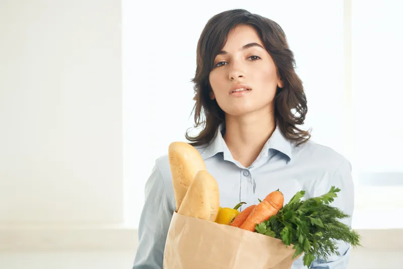 Жизнерадостная женщина держит пакет с продуктами здорового питания — овощами