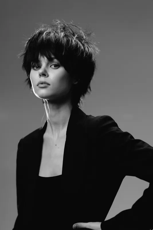 Black and white portrait of a stylish woman with short hair wearing a black blazer, showing confidence and elegance.