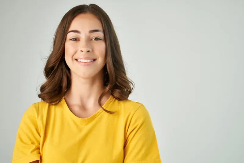 Улыбающаяся брюнетка в жёлтой футболке с модной причёской, крупный план