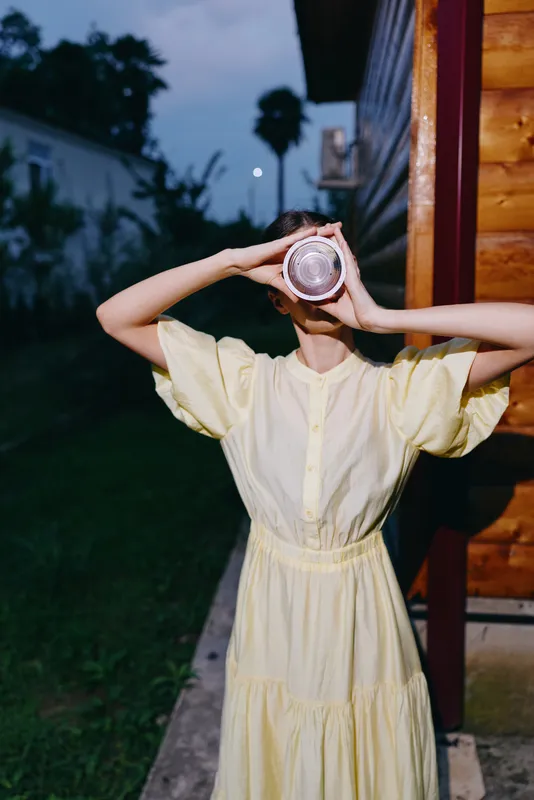 Woman in yellow dress drinks from jar outdoors at dusk authenticity inclusivity candid portrait summer evening