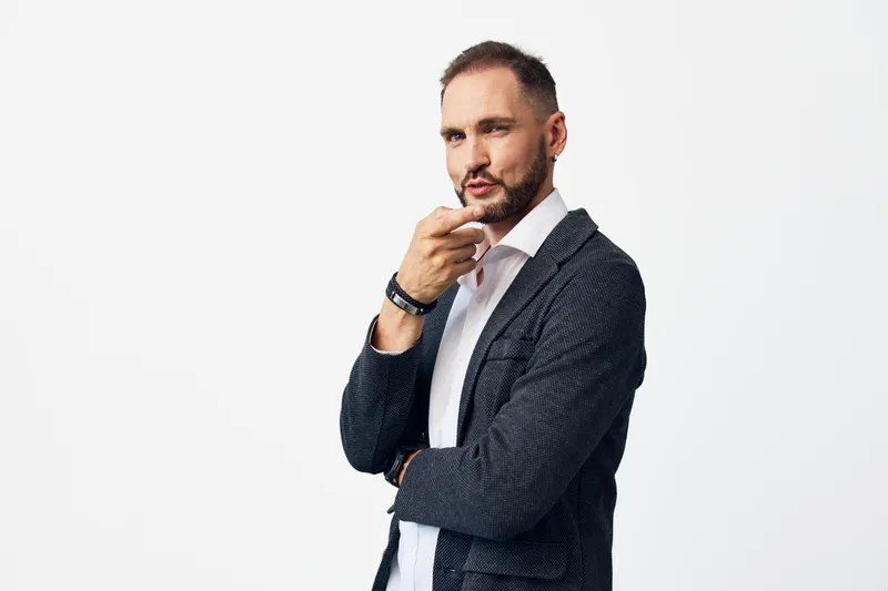 A focused business professional stands against a clean colored background, displaying thoughtful emotion. The isolated setting emphasizes confidence, strategy, and calm concentration, perfect for