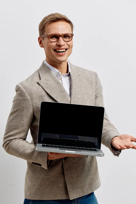 Smiling man in casual business attire holding open laptop in front of plain white background, presenting technology and communication concept, professional and friendly appearance, modern office envir