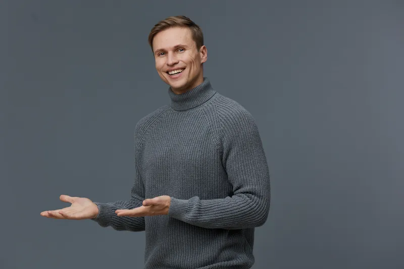 smiling caucasian man in gray sweater present gesture digital nomad casual wear isolated gray background studio portrait