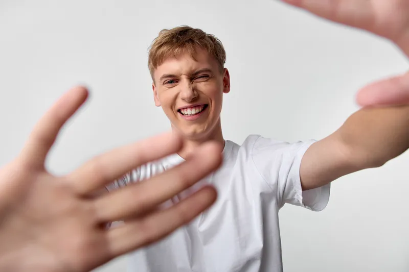 Cheerful man in a white tee reaching forward with a warm smile, hands open for a friendly greeting and connection, candid studio moment capturing approachable interaction.