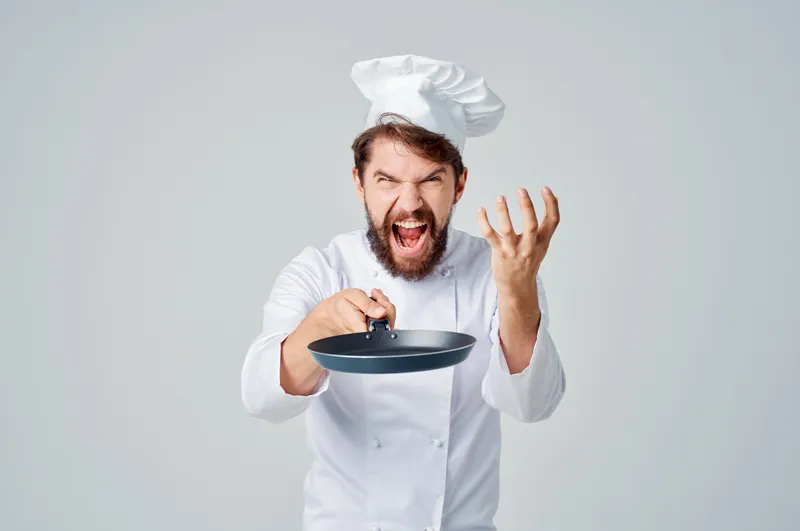 Бородатый мужчина-повар с кухонной утварью на светлом фоне