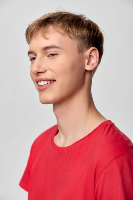 Teen male with a bright smile in a red shirt, casual and friendly headshot for youth fashion, clean pose and positive mood, studio setting, soft lighting, versatile for branding