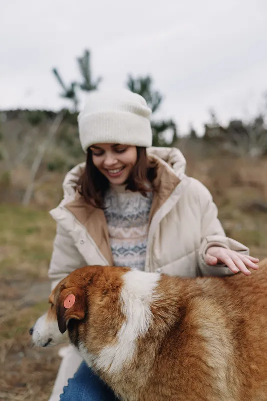 Woman with a dog outdoors in winter coat sharing affection and gentle cuddle, serene countryside setting with soft natural light and calm mood.