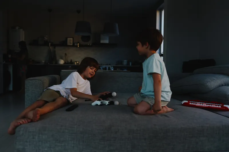 Two young boys playing together at home, enjoying their time with a video game console, laughter and excitement in a cozy setting, natural lighting.