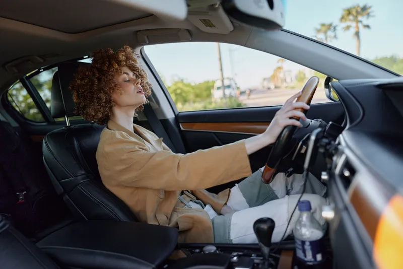 Candid woman driving a car with curly hair, wearing a beige blazer. Lifestyle scene with retro film color vibe, showcasing independence, mobility, and daily commuting.