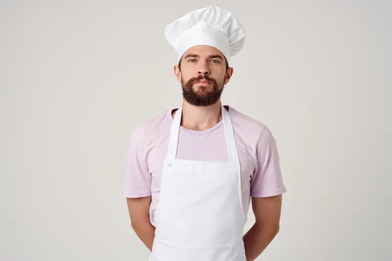 Бородатый мужчина в белом фартуке готовит на кухне ресторана