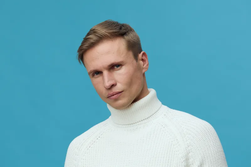 serious man wear white turtleneck sweater look camera isolated on blue background portrait mental health and gadgets concept