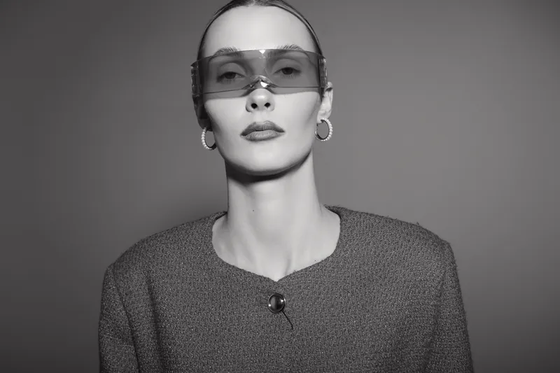 Portrait of a white woman with pale skin wearing large sunglasses and hoop earrings in a studio. Fashion concept with minimalist style and confident expression.
