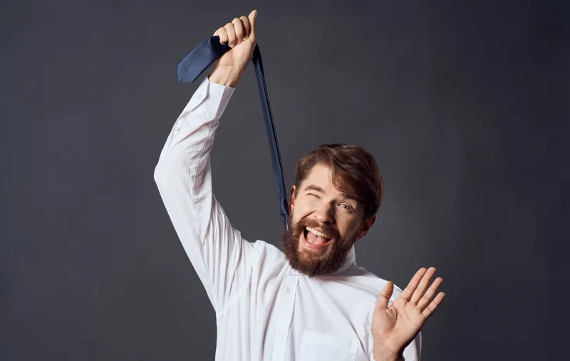 Мужчина держит галстук в руке, изображая удушение на сером фоне