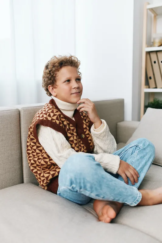 An authenticity moment features a young child at home, wearing a knit vest and denim jeans, reflecting play and curiosity in a cozy living room setting.