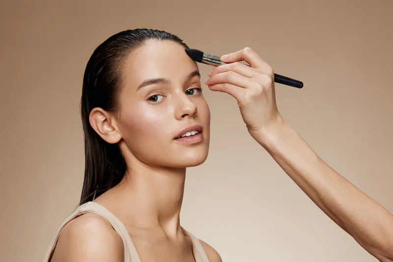 A beautiful model of Hispanic descent receiving a makeup application, showcasing natural beauty, soft lighting, and a neutral color palette, ideal for beauty and skincare concepts