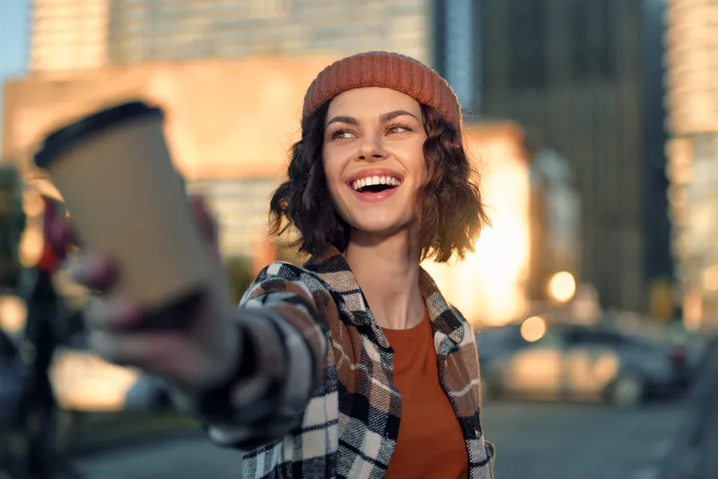 Woman smile coffee urban candid lifestyle portrait at golden hour glow, authentic moment of mindful living and emotional storytelling as a young woman offers a takeaway cup with joy.