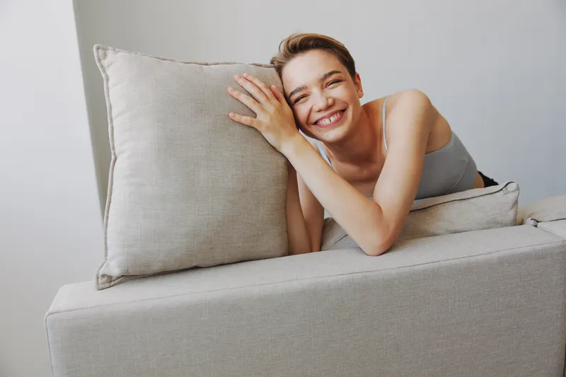 Счастливая женщина улыбается, лежа дома на диване, отдыхая в выходной день, с короткой стрижкой, без фильтров на белом фоне, свободное пустое пространство