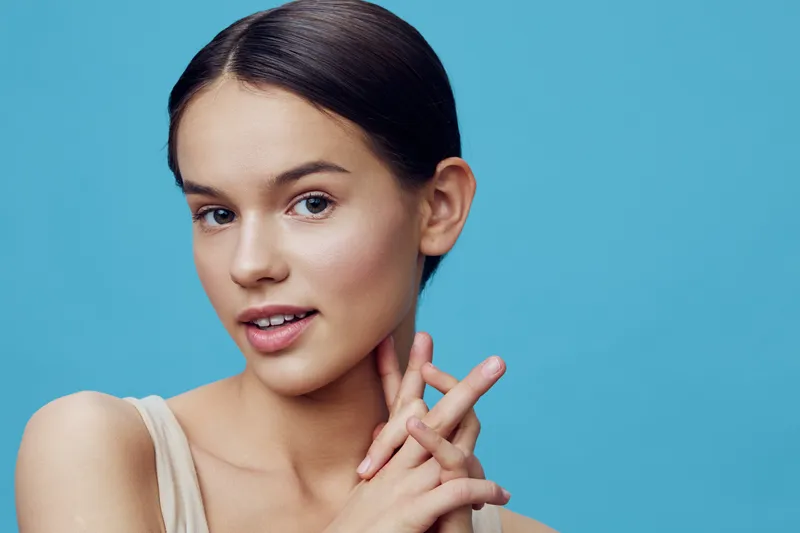 Young woman with smooth skin and a gentle smile on a blue background, showcasing natural beauty, confidence, and grace in a light fitted attire