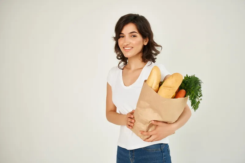 Женщина в белой футболке с пакетом продуктов для доставки на светлом фоне