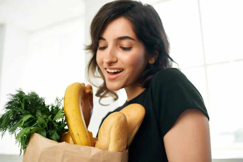 Жизнерадостная женщина с пакетом продуктов, овощами, готовит еду для здоровья