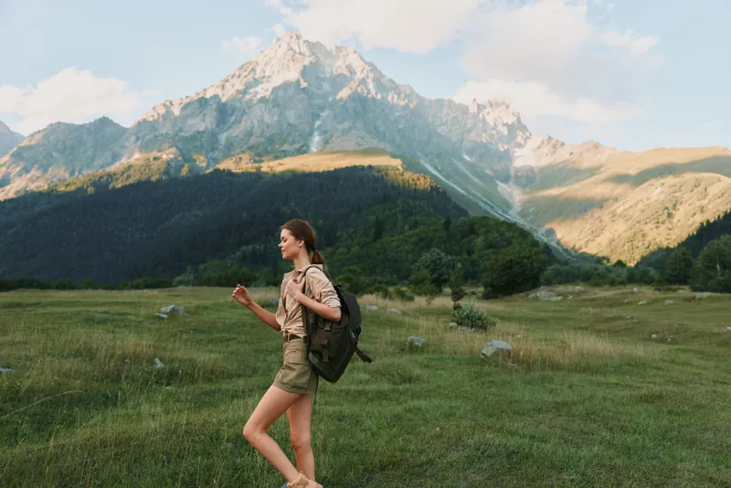 Young woman hiking in mountains, carrying backpack, casual outfit, summer day, green meadow, clear sky, active lifestyle, nature exploration, peaceful environment