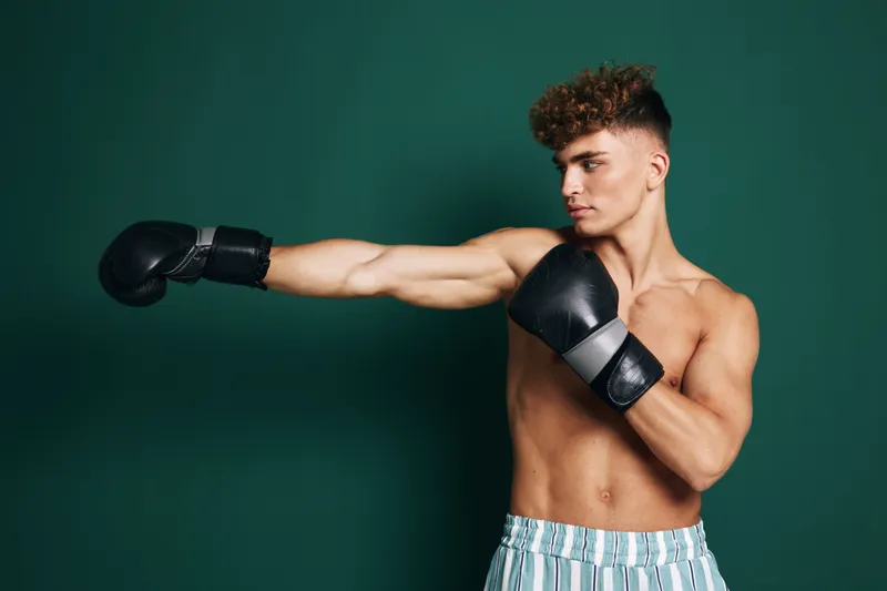 Young man with boxing gloves training and throwing a punch in studio. Athlete, fitness and workout for strength and muscle development with focused expression on face.