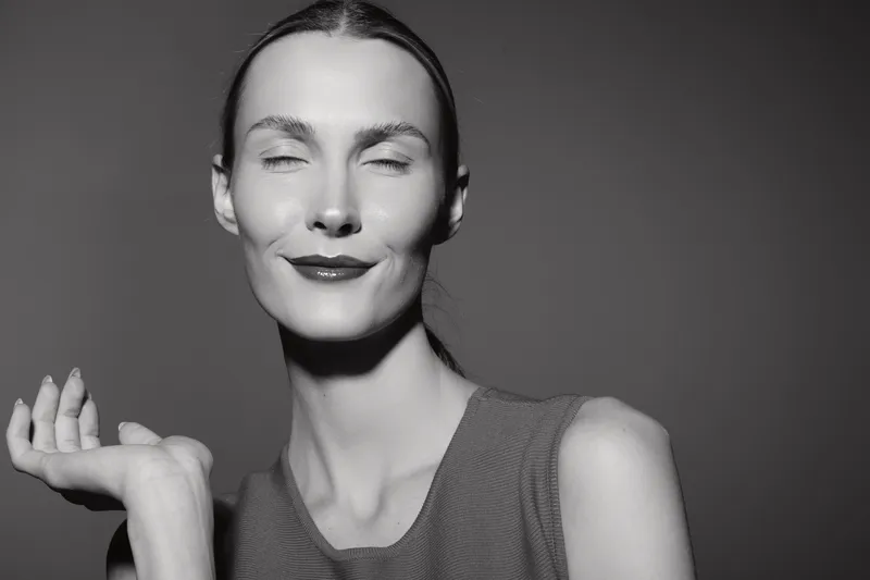 Portrait of a slim white woman with pale skin and slicked back hair smiling with closed eyes in a sleeveless top. Concept for beauty, confidence, elegance, and monochrome photography.