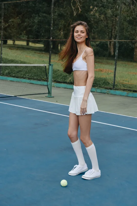 Young female tennis player in a sporty outfit, smiling with confidence on a tennis court, showcasing athleticism and style
