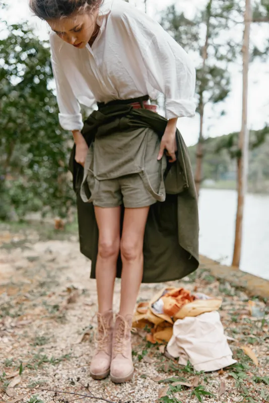 Young woman in nature adjusting her outfit reflects a casual, outdoor lifestyle with earthy tones and an adventurous spirit, showcasing a connection with nature
