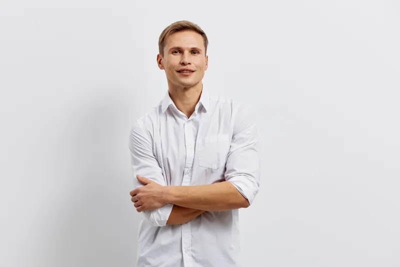 Smiling young man with short light brown hair in casual white shirt stands isolated on plain white background. People lifestyle concept, happy, confident, relaxed, casual style, positive emotion, stud