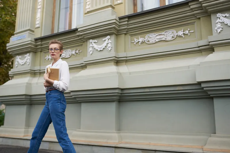 Симпатичная женщина-модель в джинсах с книгой в руке возле здания на улице