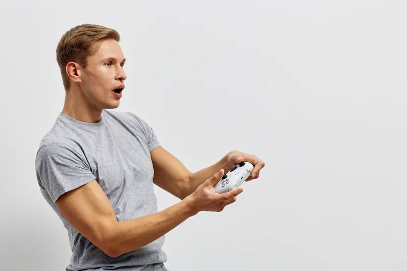 surprised young caucasian man play video game hold gamepad isolated on plain white background casual wear focused facial expression digital entertainment concept