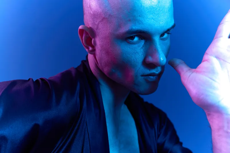 A striking portrait of a man against a vibrant blue backdrop, showcasing an expressive pose and bold lighting, captured in color and emphasizing emotional intensity.