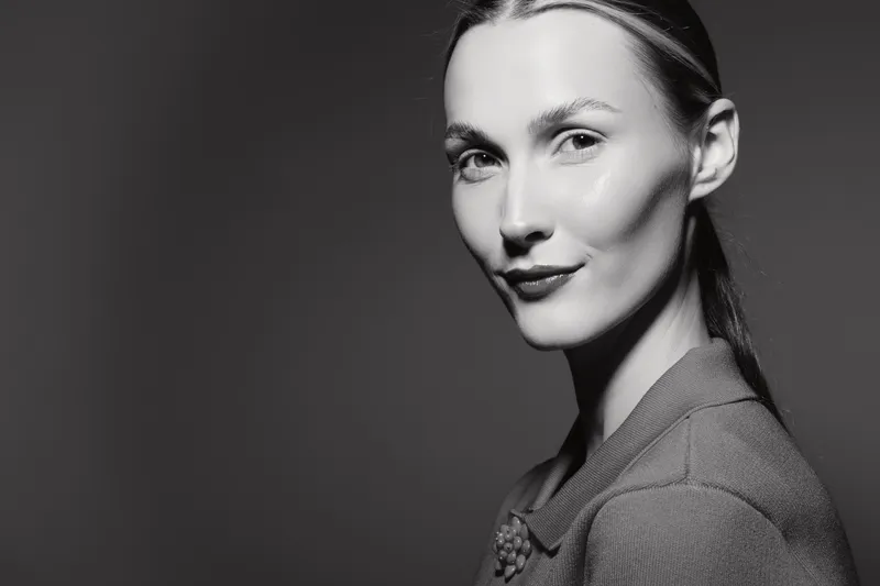 Portrait of a young Caucasian woman with fair skin and straight hair smiling softly against dark background. Concept of elegance, beauty, and confidence.