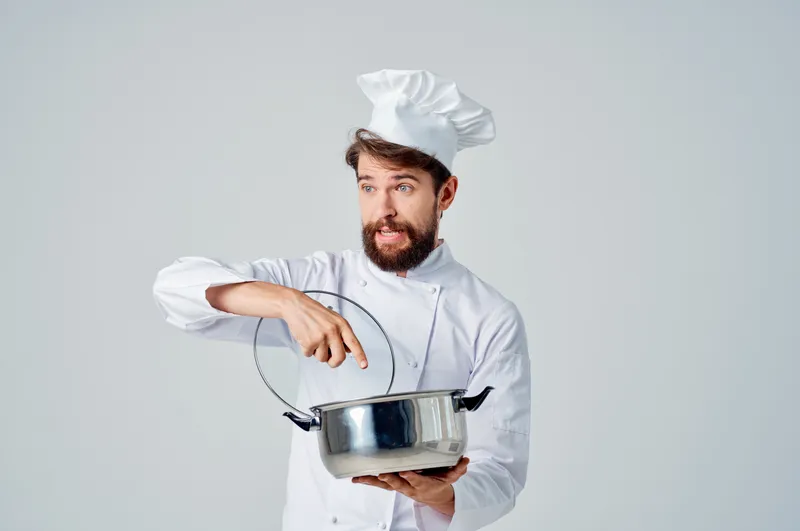 Весёлый повар держит в руках кастрюлю на кухне, занимаясь приготовлением пищи на светлом фоне