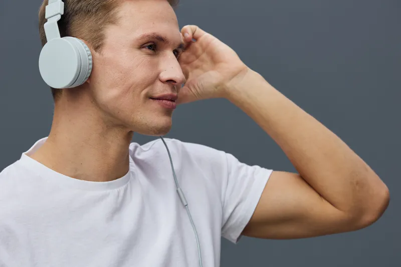 young caucasian man with headphones listen music relax mental health mindfulness concept casual white t-shirt gray background studio portrait
